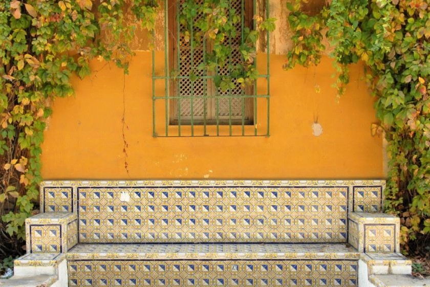 an ornately decorated stone bench in front of a bright yellow wall