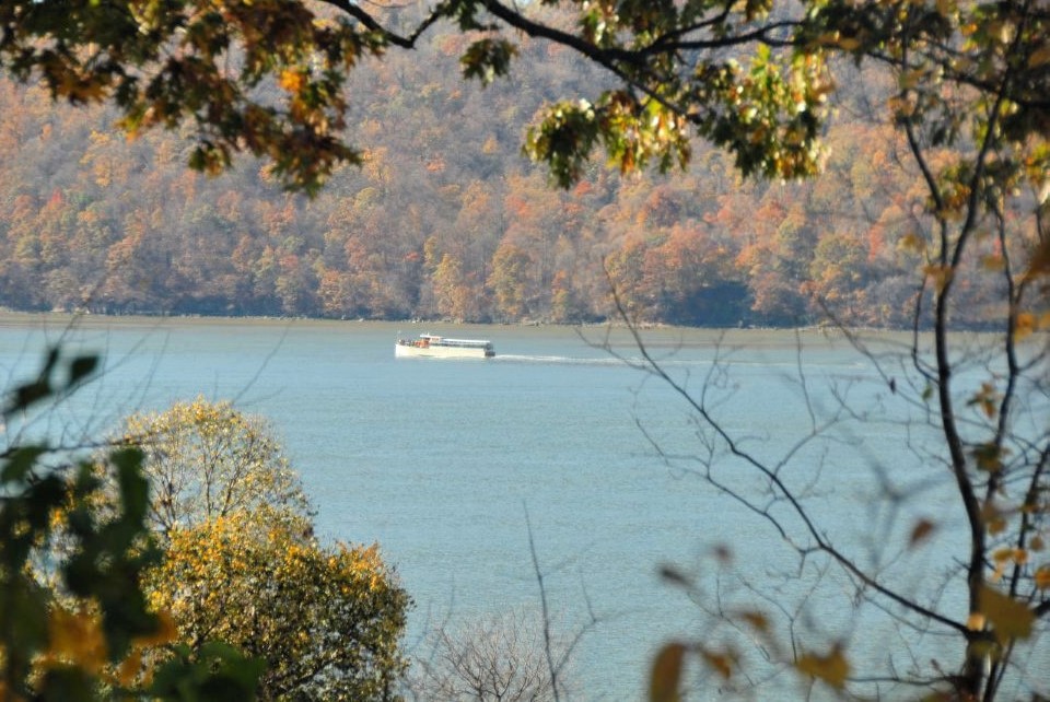 a motor boat skims over a blue lake with orange Autumn foliage on the shores in the foreground and background