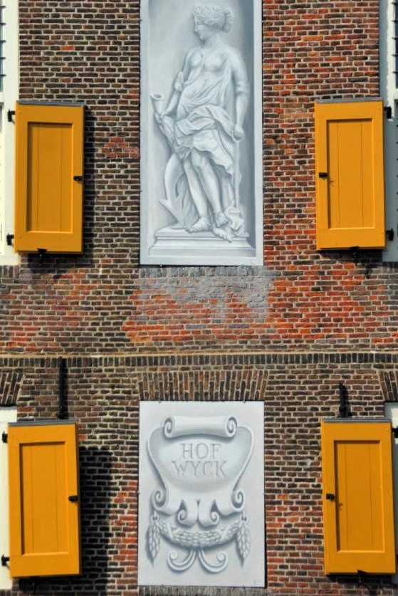 a close-up photo of the red brick facade of the Hofwijck mansion, with bright orange shutters and two intricately painted plaques