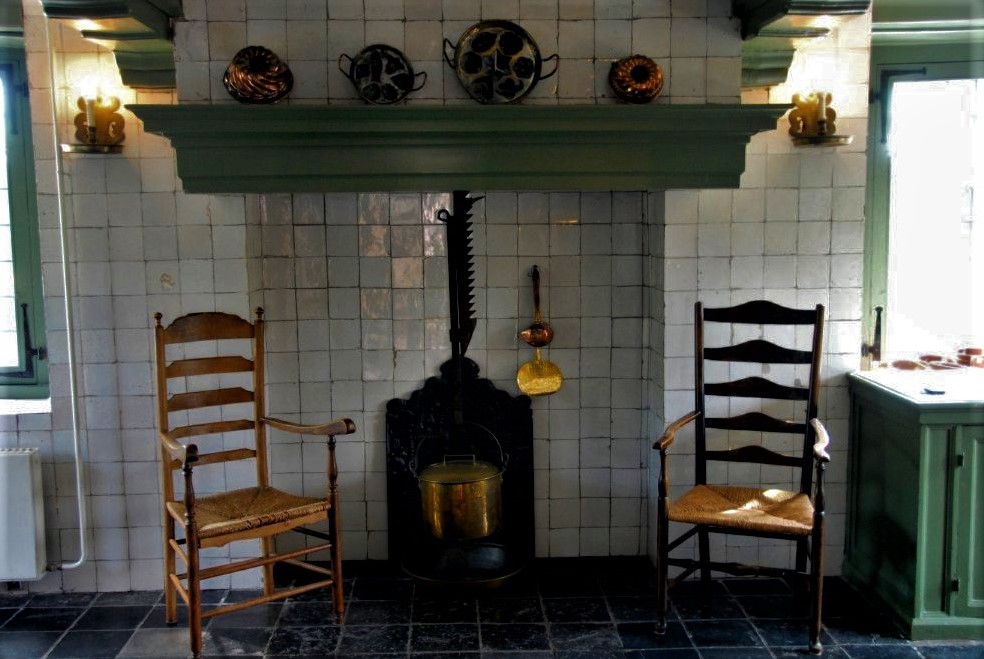 two antique wooden rockingchairs sit side by side before a cast-iron stove in a traditional Dutch kitchen
