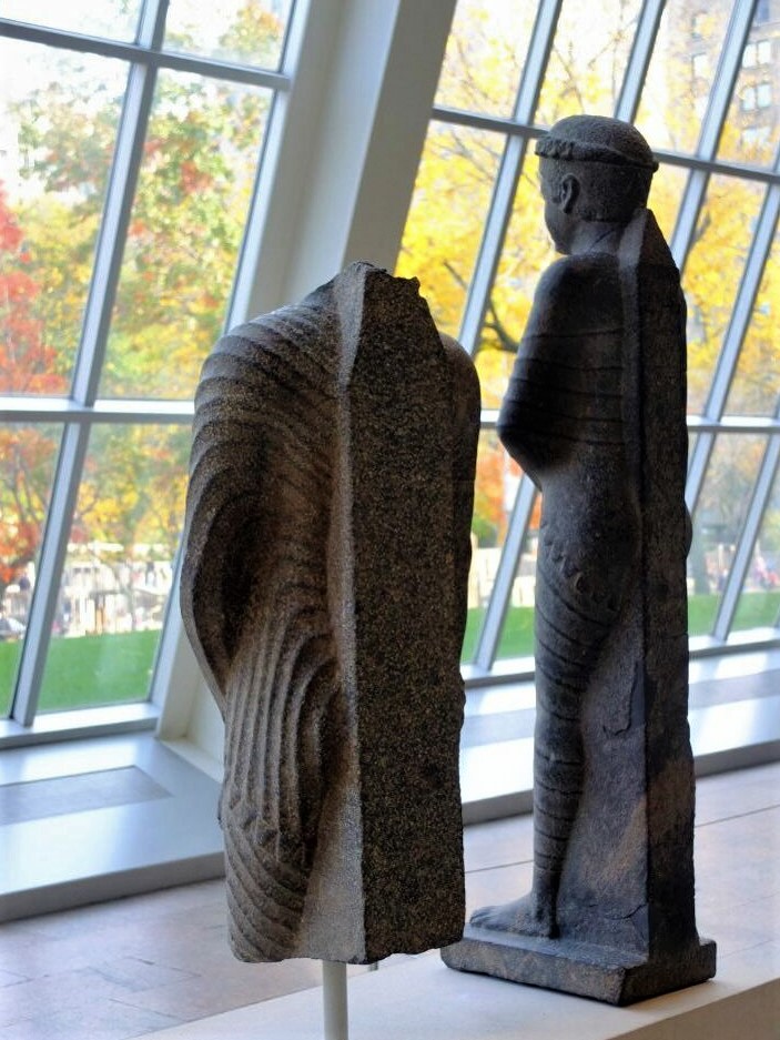 two ancient stone statues facing toward the wall of glass windows