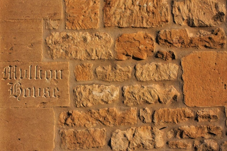 a tan stone wall with a stone plaque embedded, in which is carved the words Mullion House