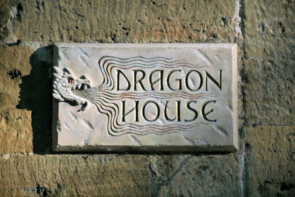 a stone plaque with carved letters reading Dragon House. A carved illustration of a dragon winds around the words.