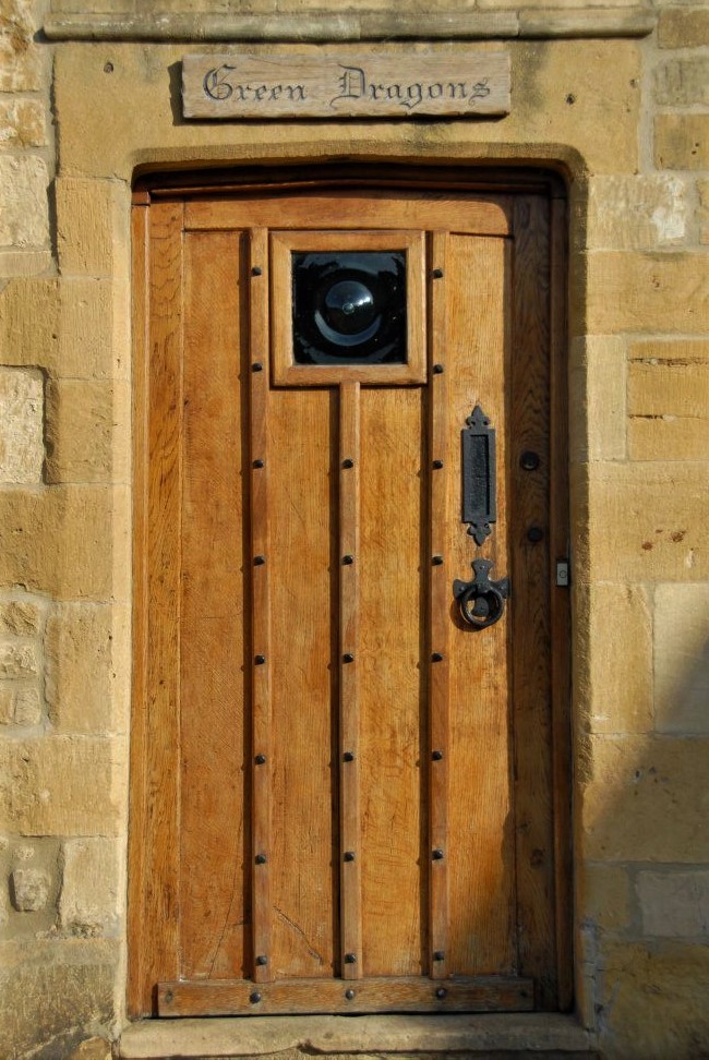 an old wooden door in a stone wall, above which reads in a carved stone plaque, Green Dragons