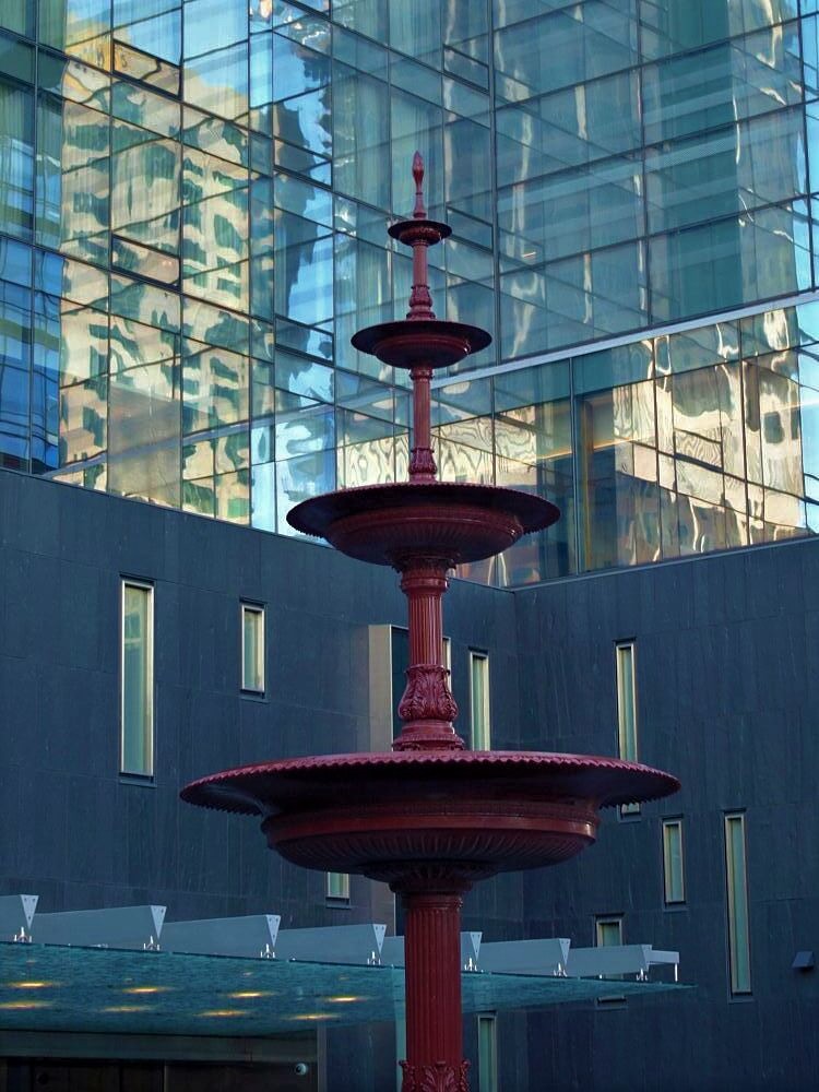 A shadowed fountain surrounded by gleaming skyscrapers