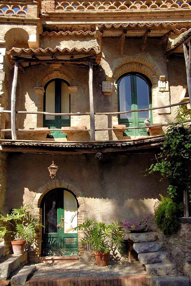 An old, two-level terracotta house with a curving wooden balcony on the top floor