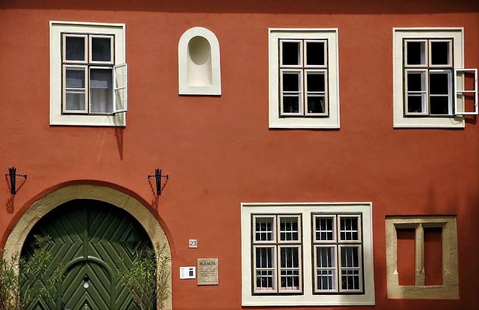 A russet building with white framed windows and a dark green arched door