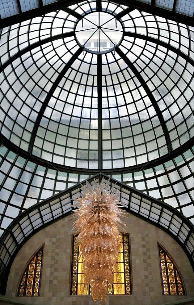 A glass dome from which hangs an intricate glass chandelier