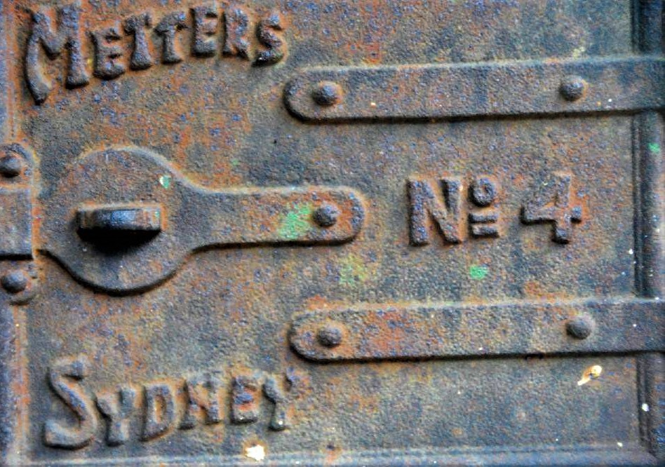 The rusted metal door of an antique safe, featuring words that read 'Metters No. 4, Sydney'.