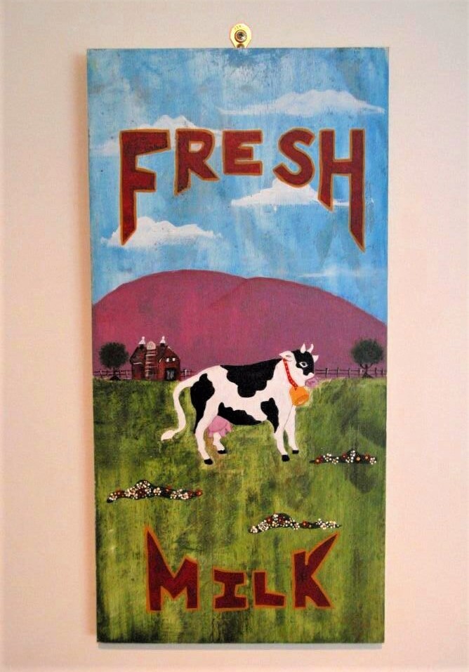 A hand-painted sign that reads 'fresh milk' and features a black and white cow grazing in a green pasture