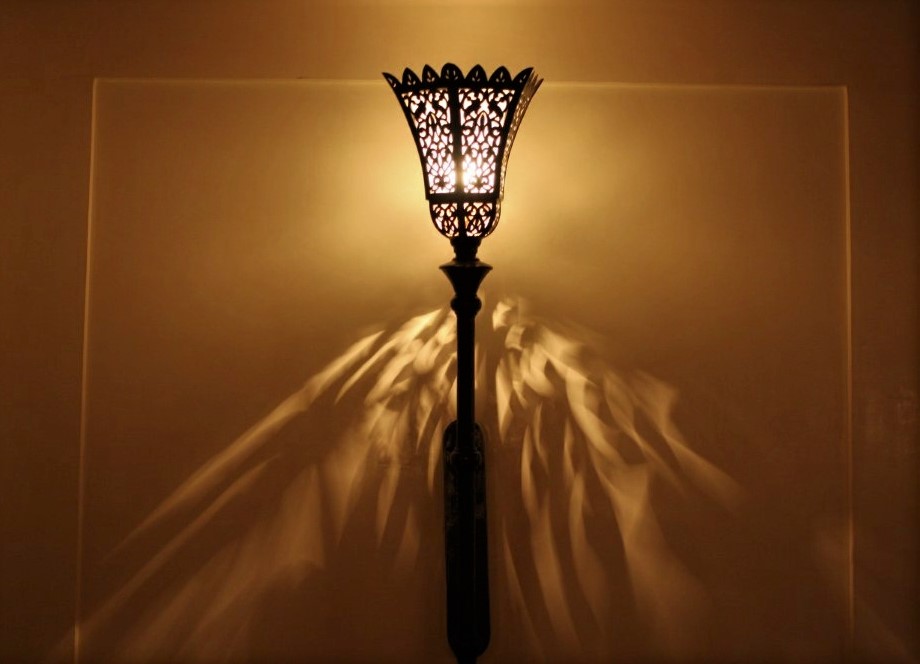An illuminated lamp in an ornate metal sconse which splashes light on the golden wall behind it