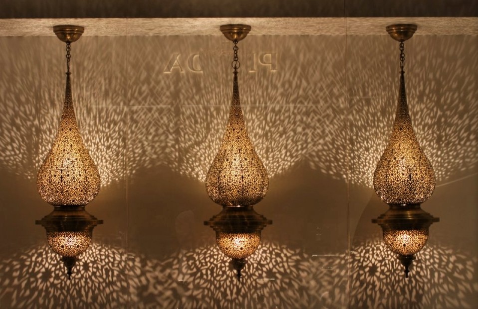 Three illuminated, intricately designed lamps with golden metal shades which throw light across the walls behind them