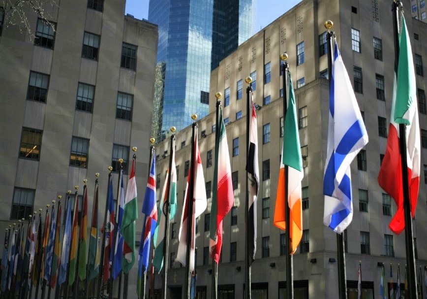 A row of international flags in the foreground against distant skyscrapers
