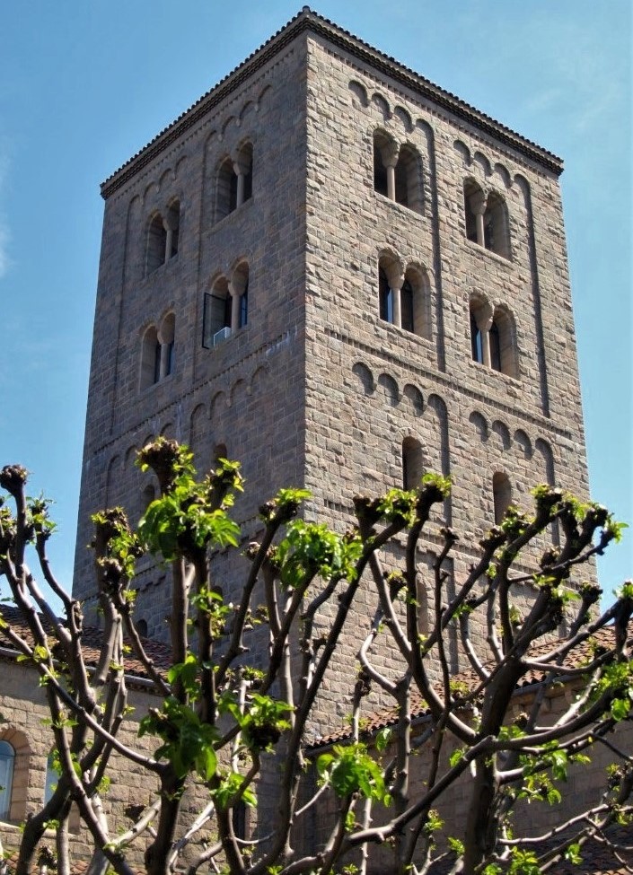A tall stone bell tower framed by trees in the foreground