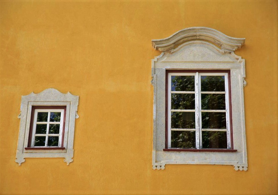 A mustard-yellow terracotta wall with two ornate windows, one larger than the other