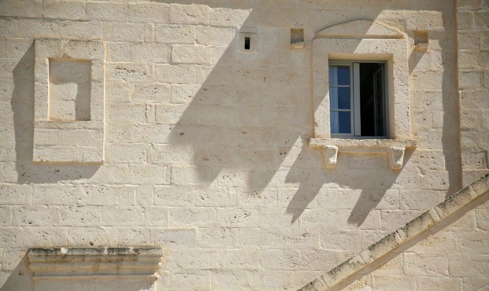 A beige stone wall with a small square window