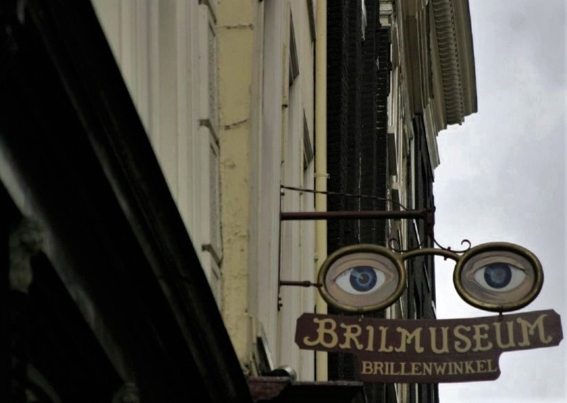 A sign hanging from a shop front featuring two large bespectacled eyes