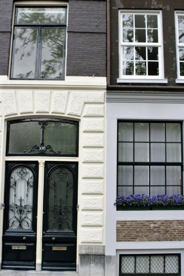 The front of a narrow stone building with purple flowers in the window box