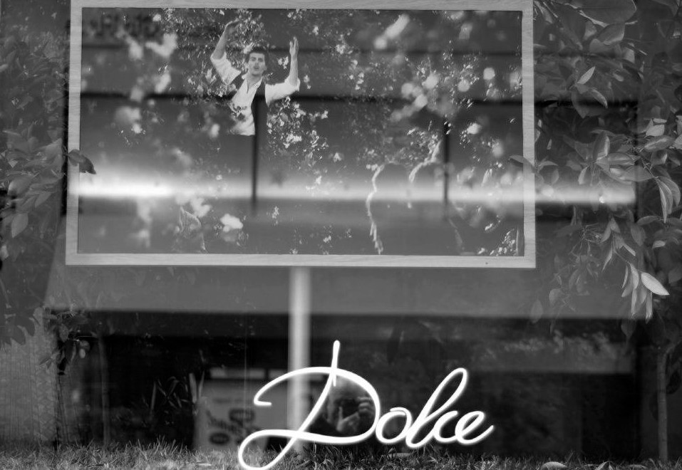 A window with a sign that reads, dolce, reflecting a man across the street