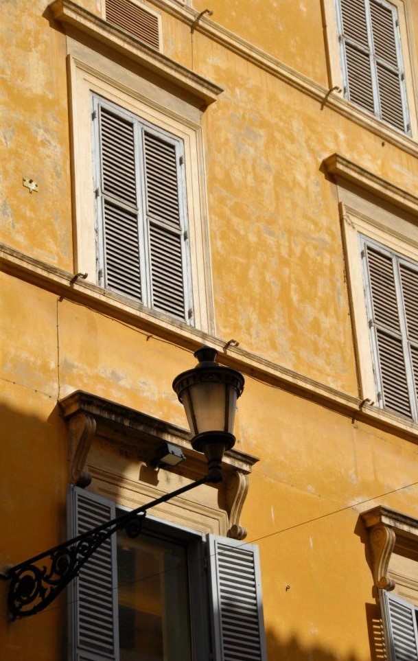 The side of a stone building featuring a wrought iron gas lamp