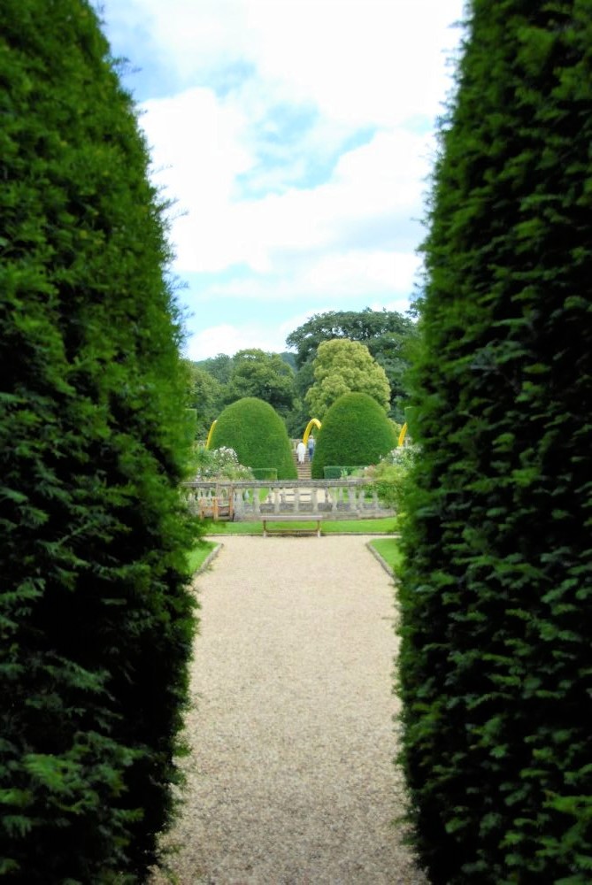 Two neatly trimmed bushes, through which can be seen a pathway in an English garden