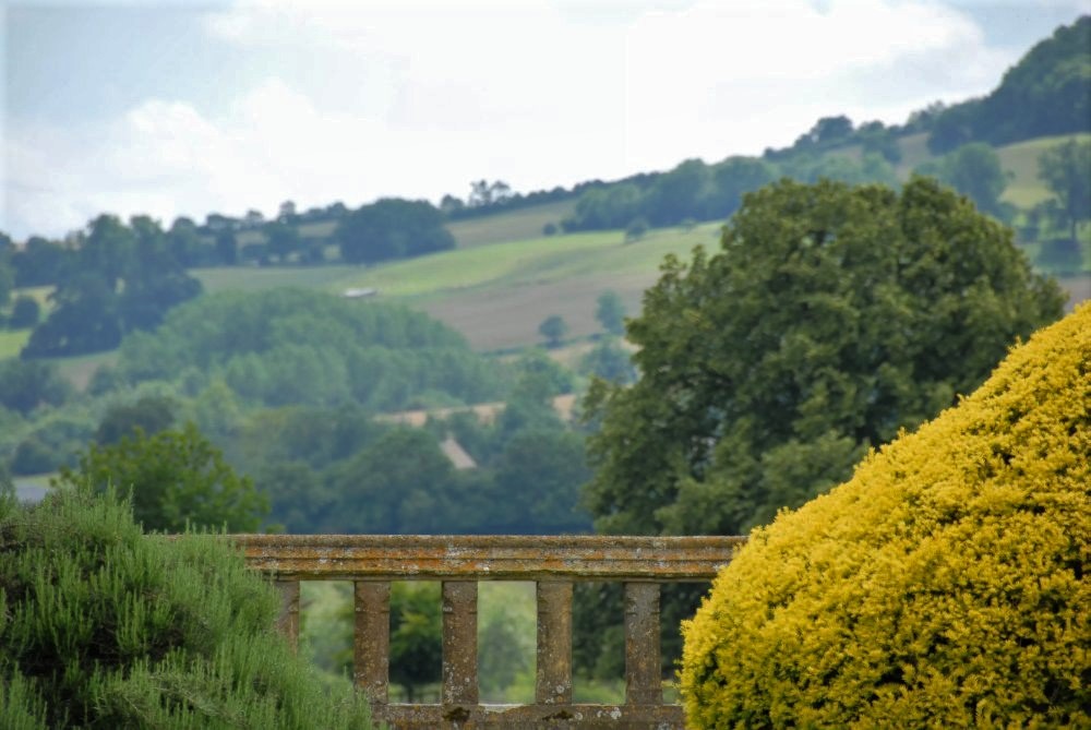 A stone railing in an English garden, with a lush green hillside visible in the distance