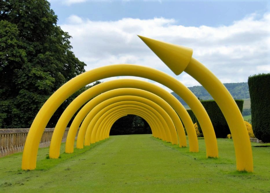 A sculpture of a yellow spiral half submerged in the ground, creating a tunnel