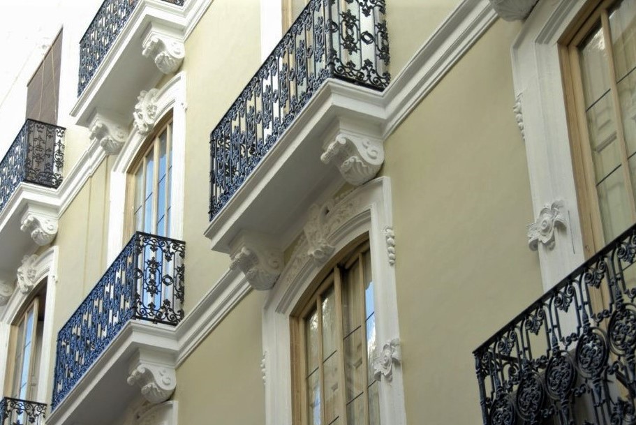 A pale green apartment building with ornate iron balconies viewed from below