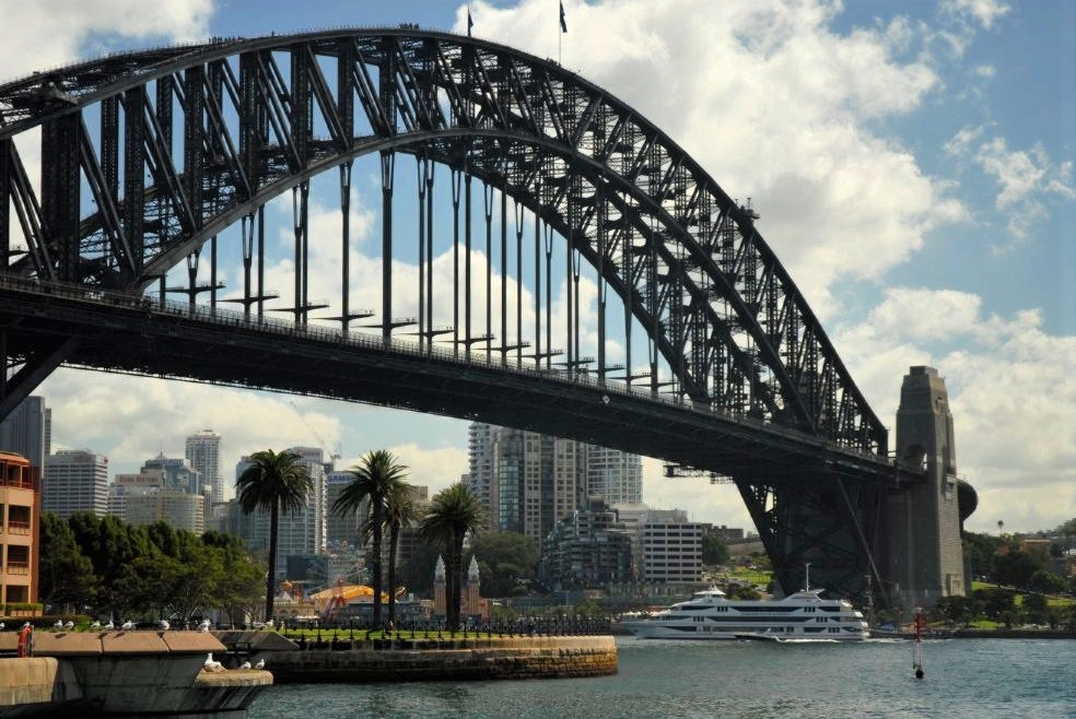 The Sydney Harbour Bridge spanning above the water, with palm trees on the shore