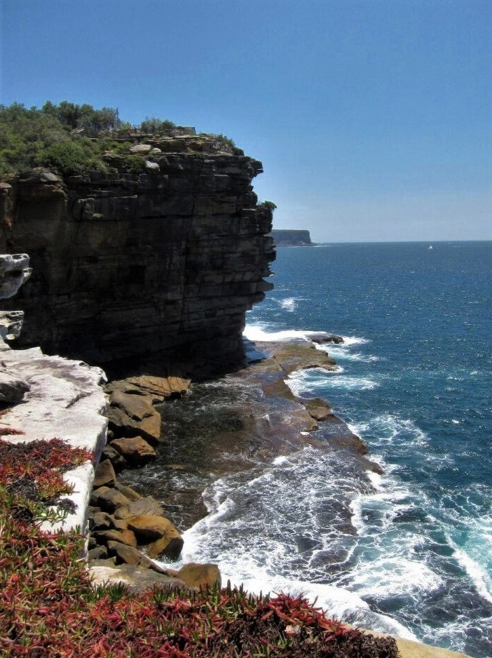 A steep cliffside which drops off to a stony beach and crashing ocean waves