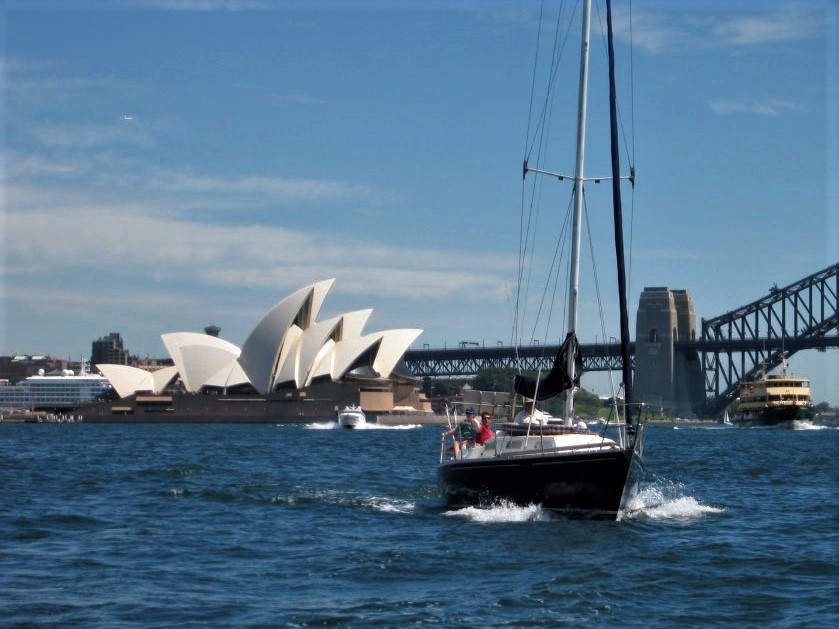 A sailboat gliding in Sydney Harbour with the Sydney Harbour Bridge and opera house in the background