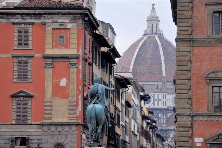 A statue of a man on a horse with the Duomo visible in the distance among brick buildings