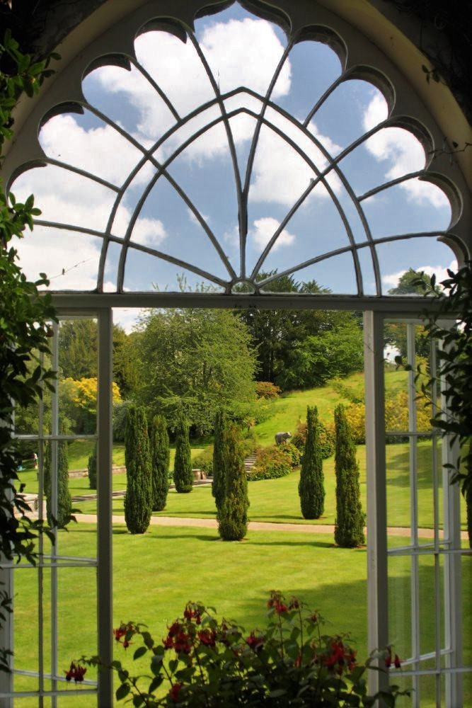 An ornate window through which a vibrant manicured garden is visible