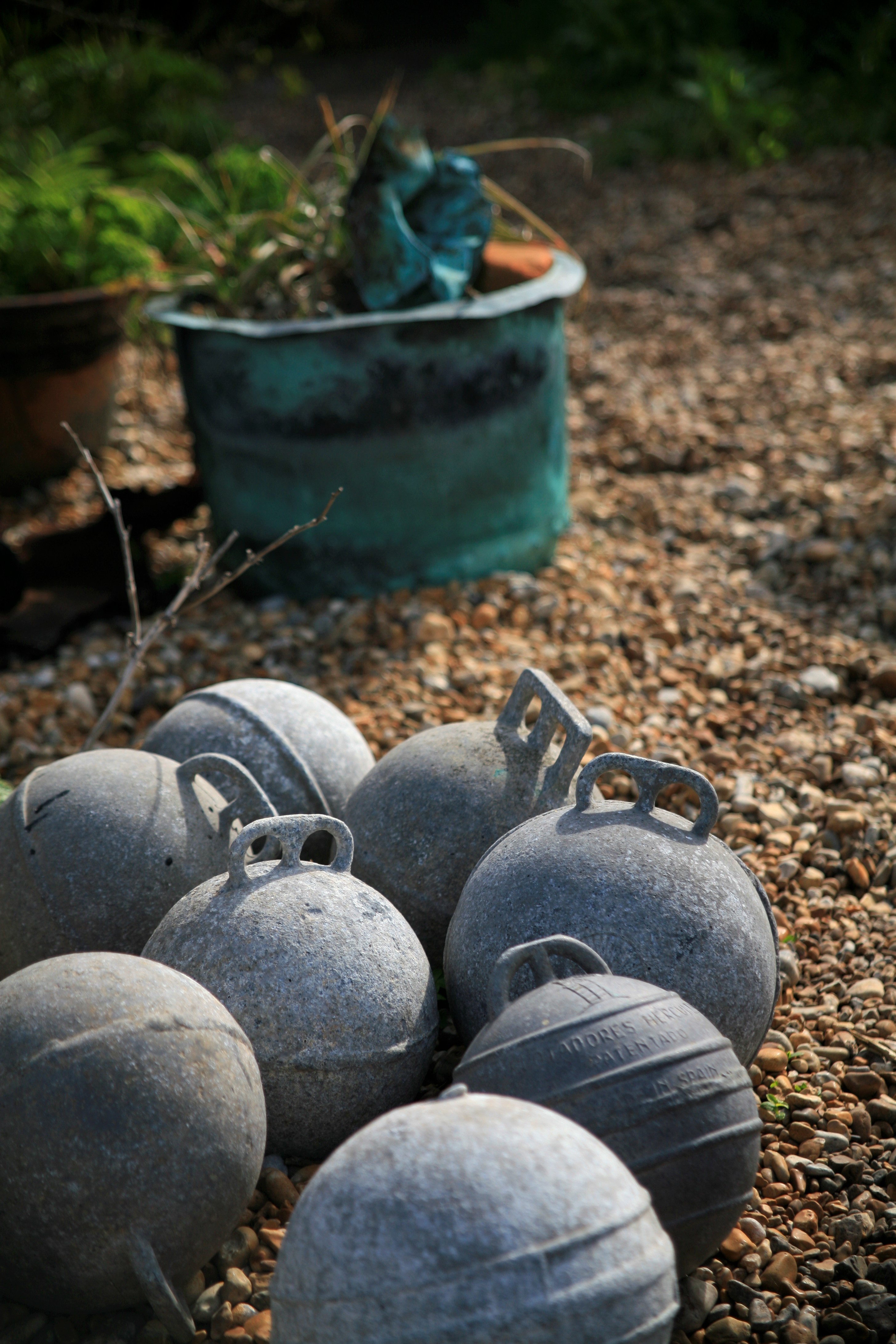 A cluster of buoys sit beside a blue bucket on gravel