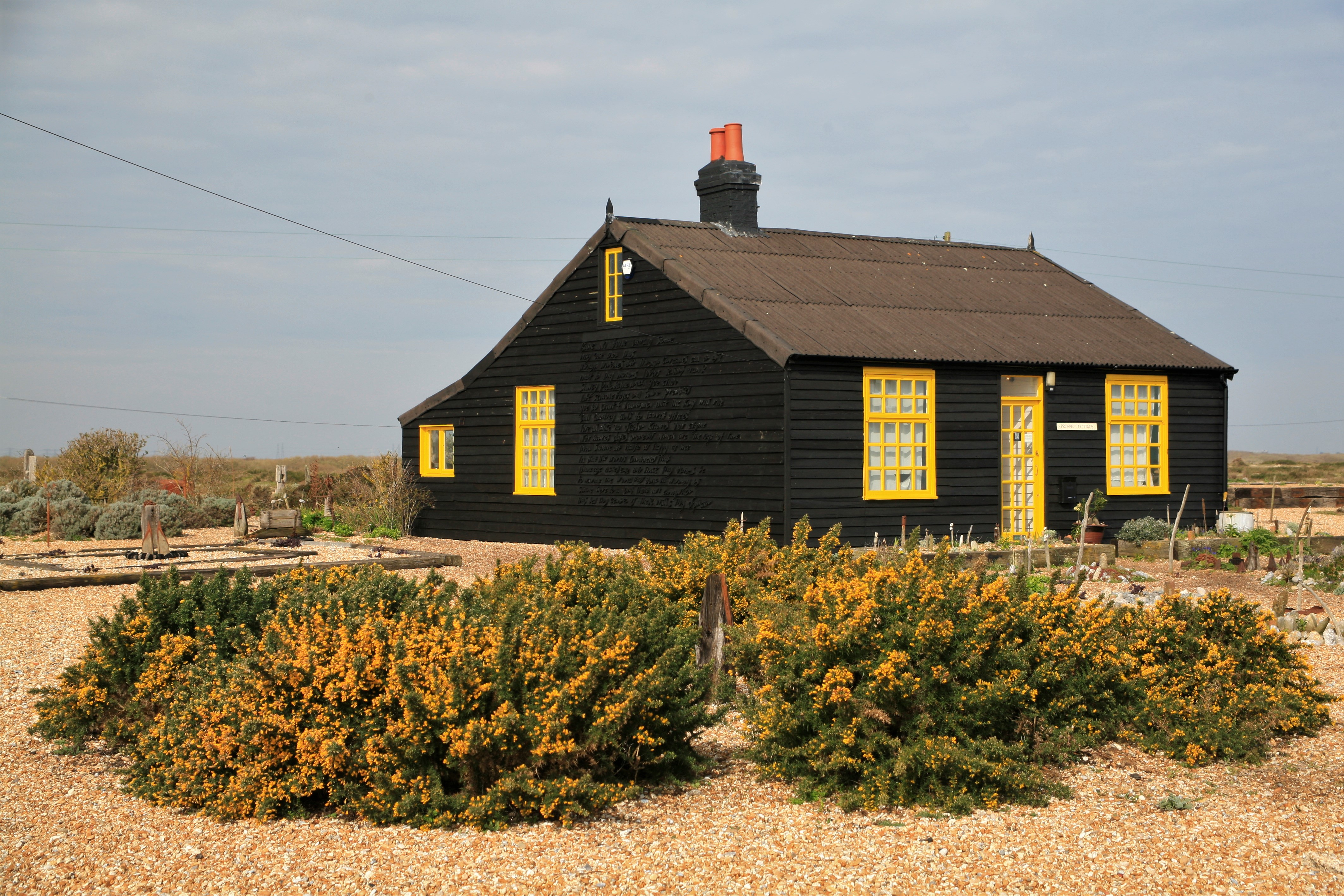 A black and yellow seaside cottage surrounded by gravel and bushes