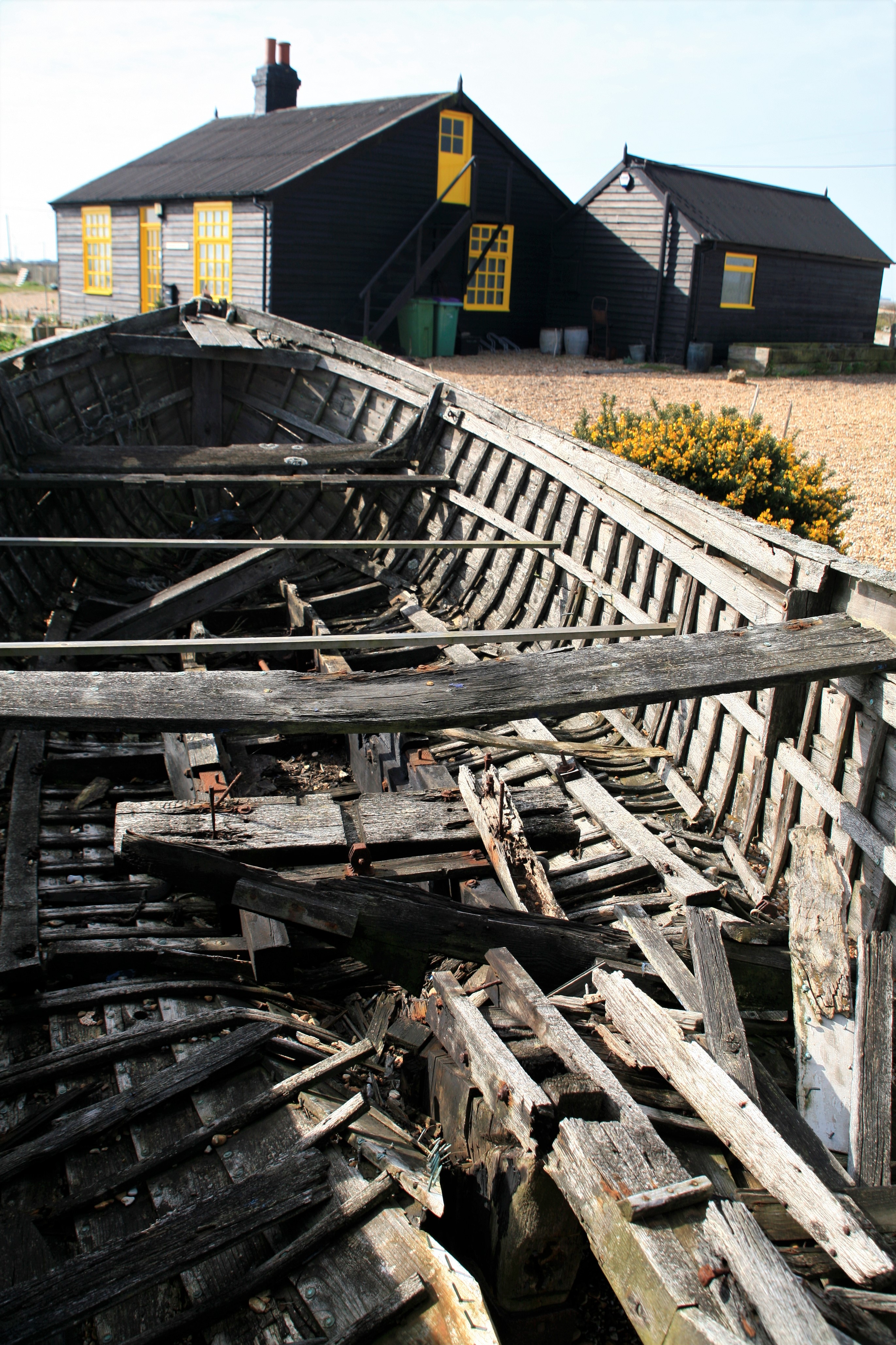 A weathered wooden boat viewed from the stern, with a black and yellow cottage visible in the distance
