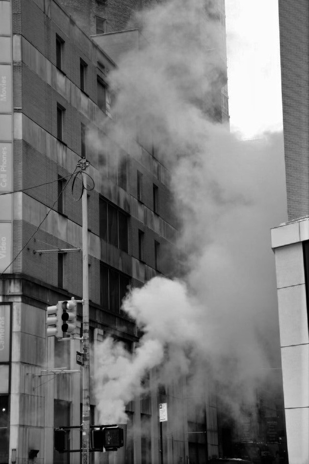 A black and white photo of steam rising from the ground on a city street