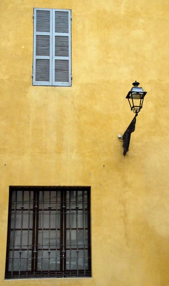 A golden yellow stone wall with two windows and a lamp