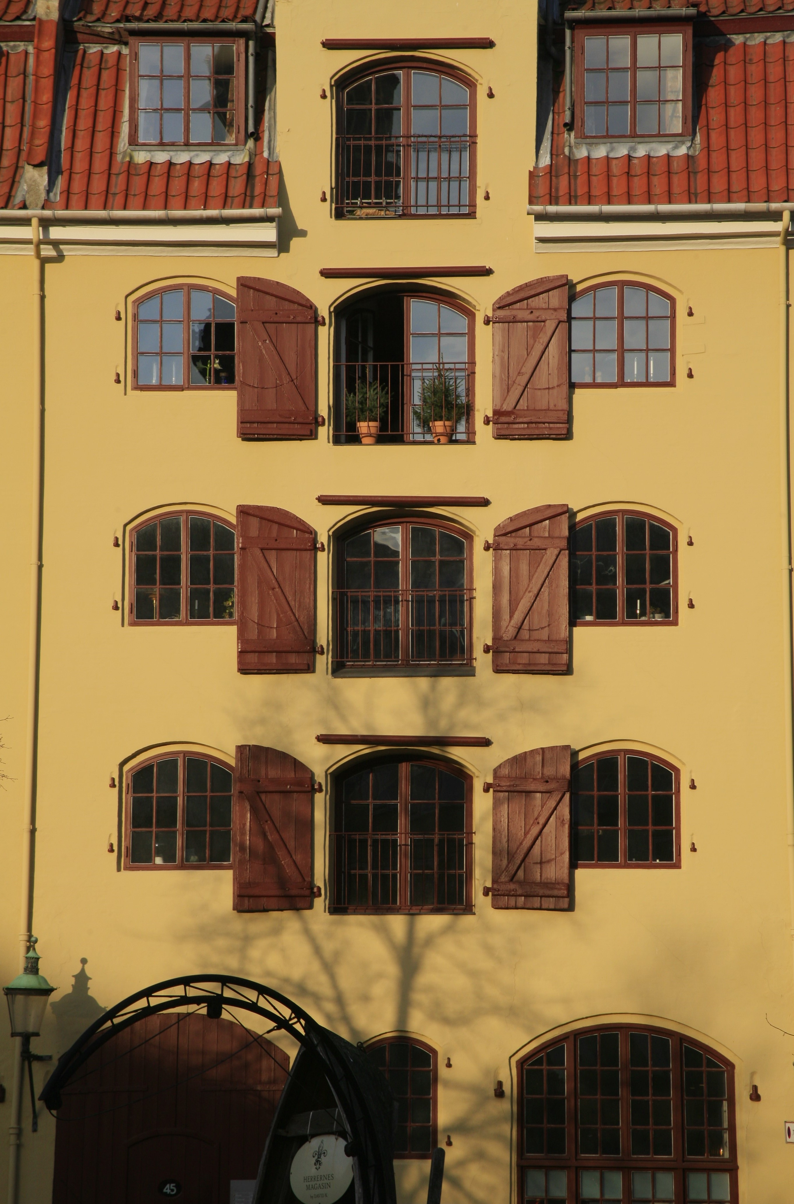The facade of a yellow, narrow house featuring arched windows and wooden shutters