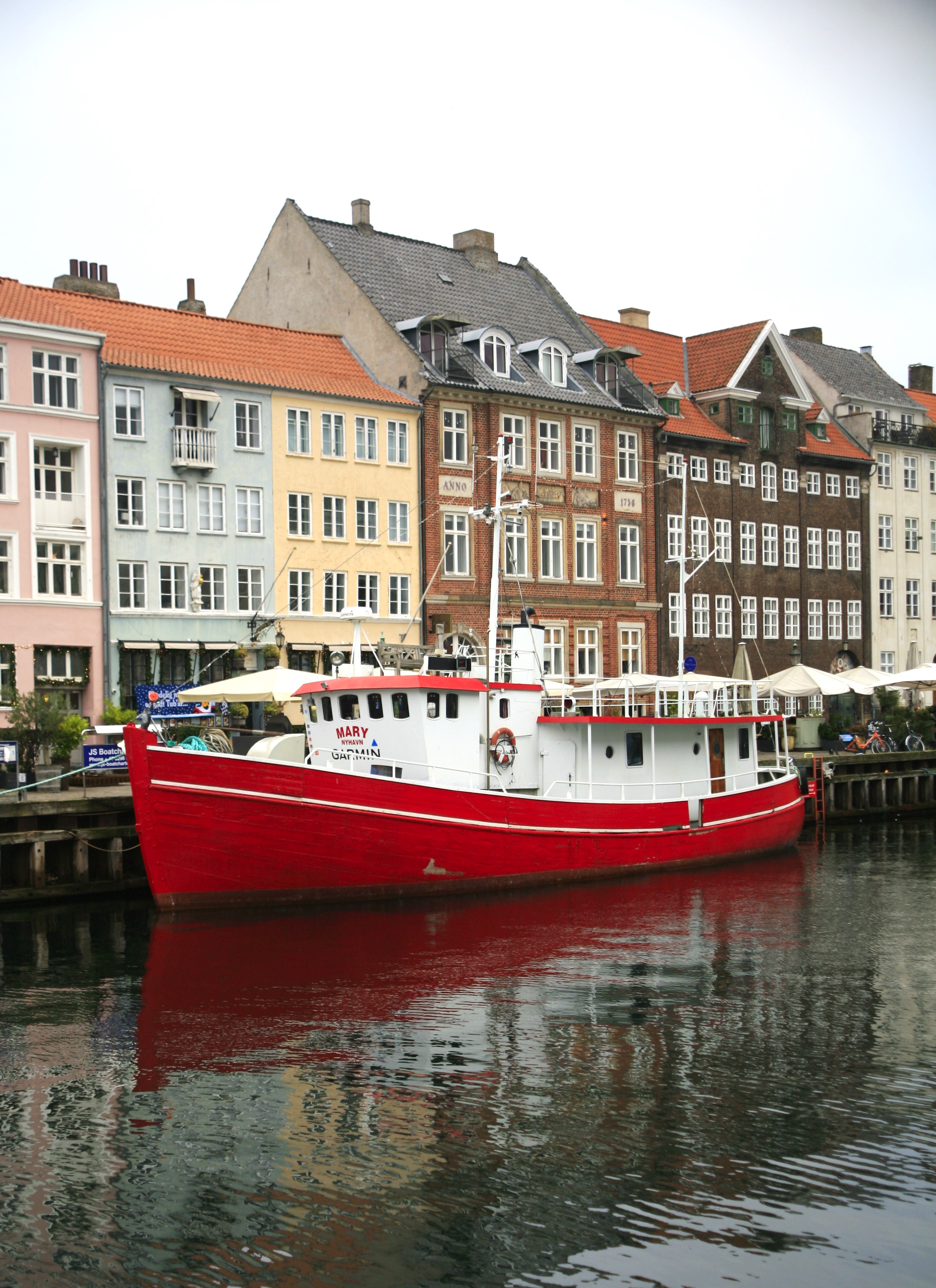 A large red sailboat docked at the Port of Copenhagen with colourful houses visible in the background