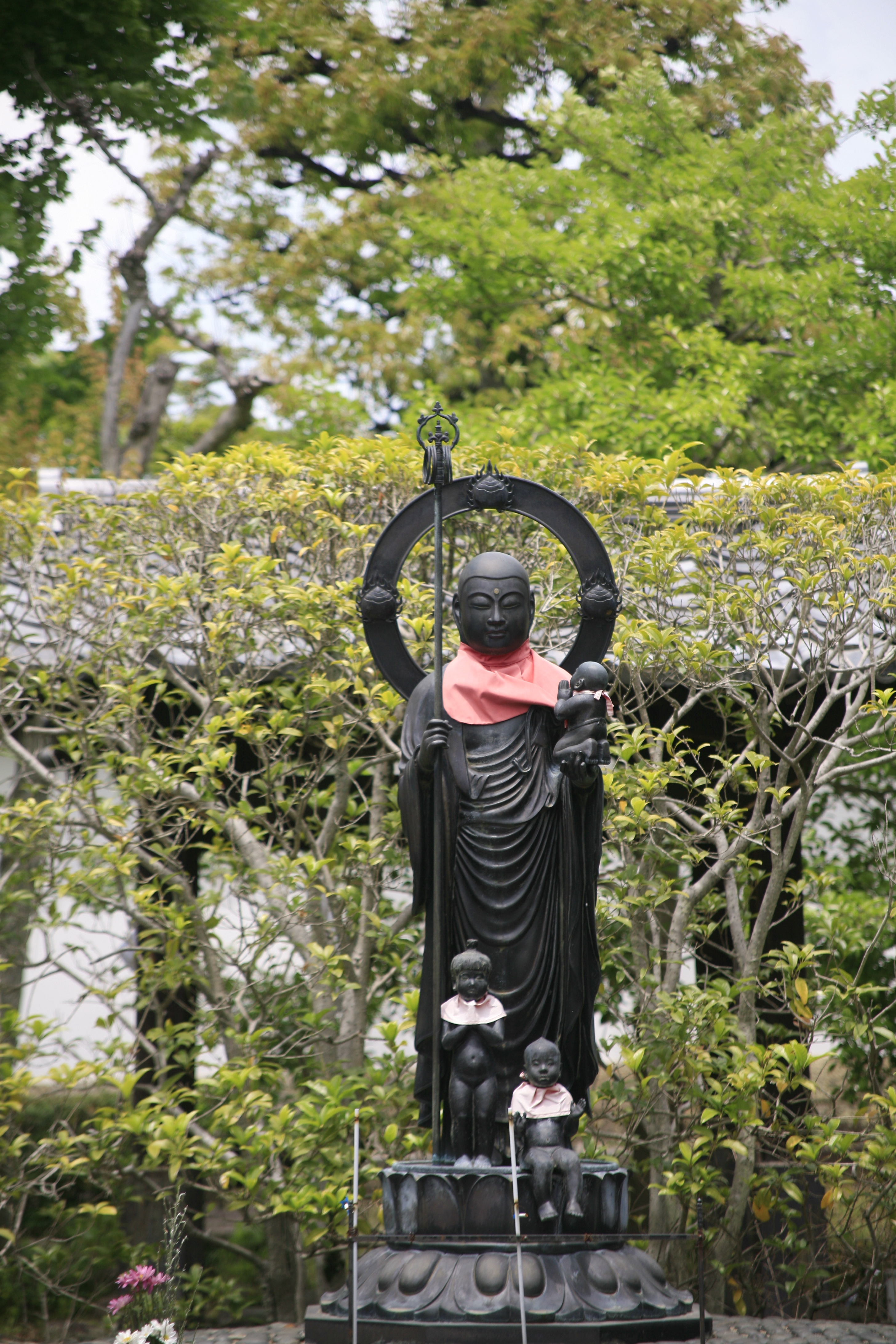 A stone Buddha stands among green foliage
