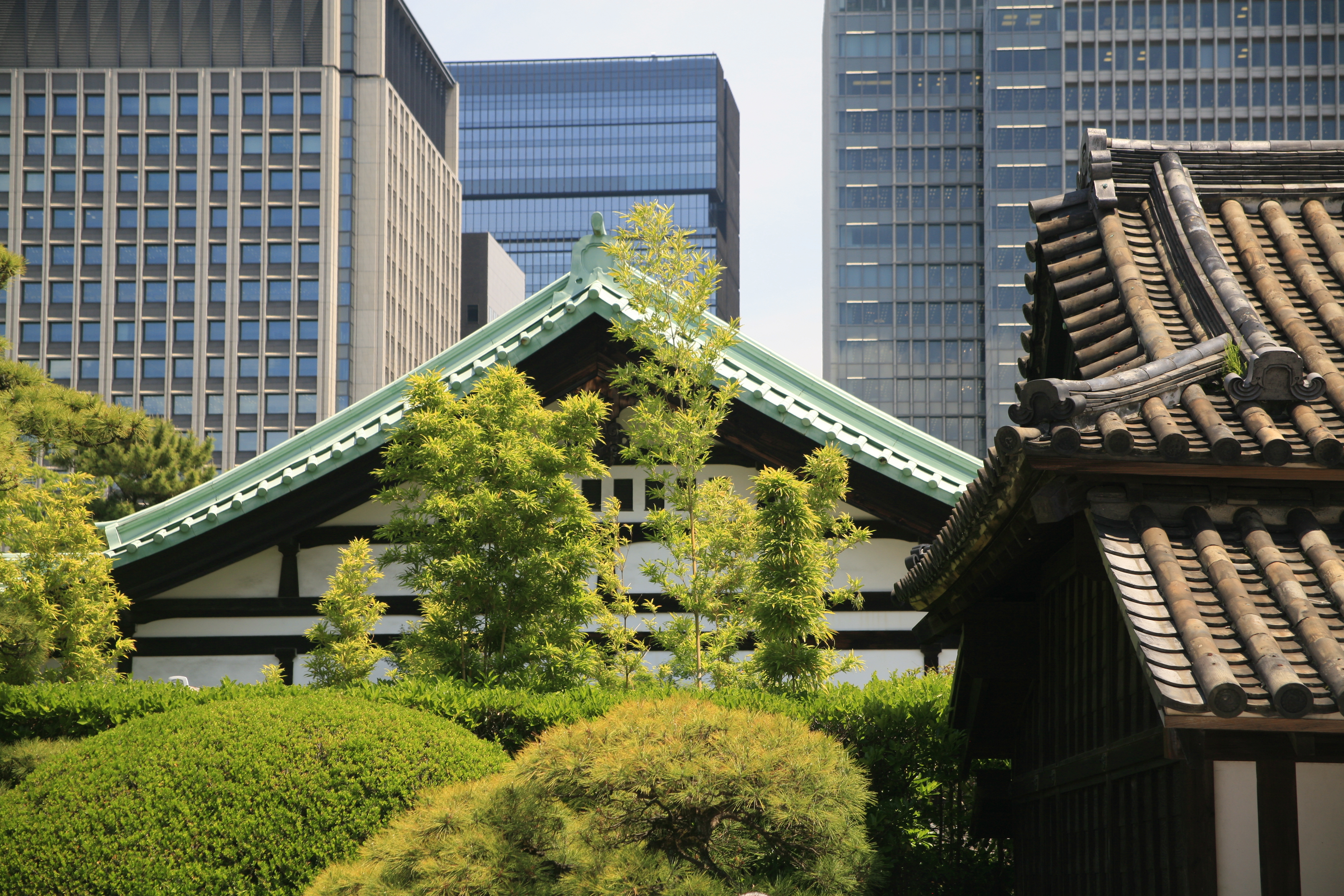 A mint coloured roof of a pagoda is visible amongst green vegetation, with skyscrapers visible in the background